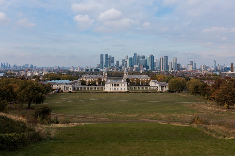 A wide view of a historic white building with classical columns and symmetrical towers, situated on a well-maintained grassy park area with a few visitors and minimal landscaping. The building feature